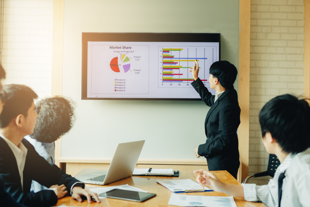 inidividual in business suit addressing group presenting using a screen with images, appears to be Asian