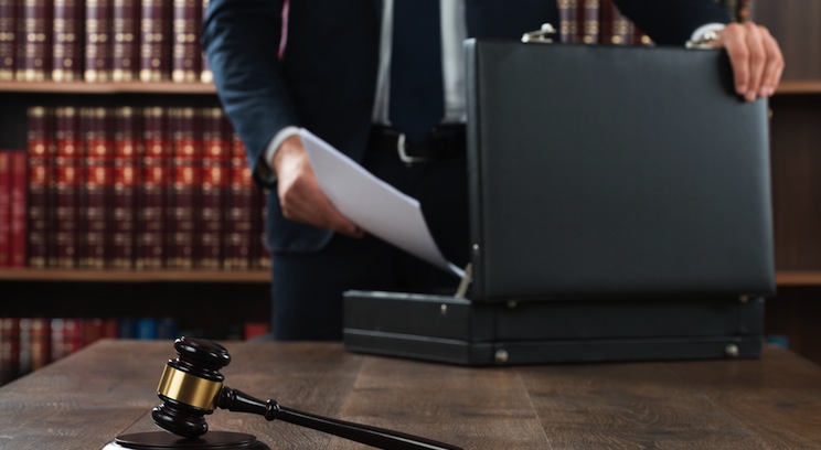 a person in a suit putting papers in a briefcase. a gavel is in the foreground