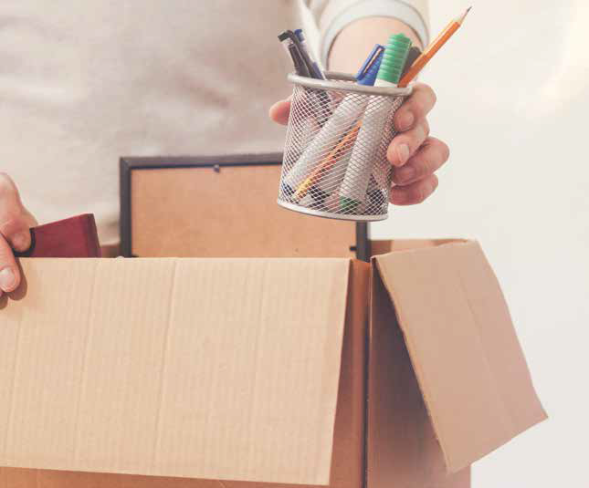 a hand putting a cup of pens in a cardboard box