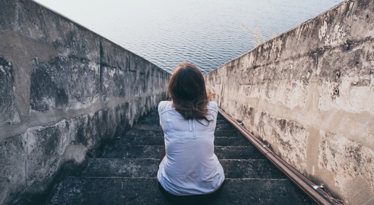 an image of a person sitting on stone steps leading to a body of water