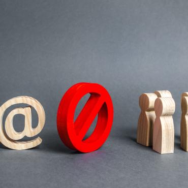 illustration or photo of what appears to be wood figures - on the left an at (@) sign, in the middle the universal sign for something being prohibited, a red circle with a slash inside, and to the right, figures representing people 