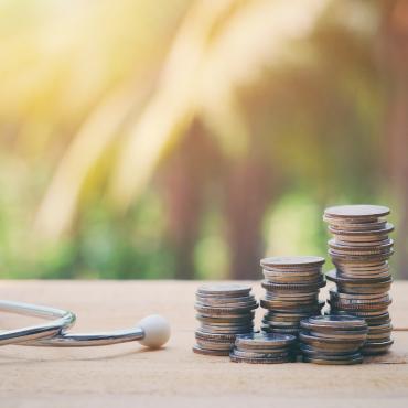 Close up of a stethoscope and stack of coins on an old wood table. 