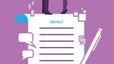 Two people stand on top of a contract and shake hands. 