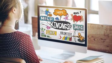 A woman looking at her computer which is full of positive messages: Hope, Help, Kindness, Share, Volunteer, Thank You.