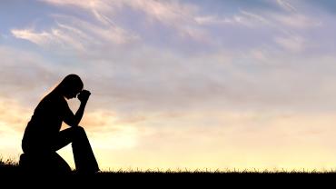 women with head in hands in front of sunset