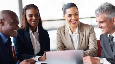 four diverse professionals seated at a table smiling