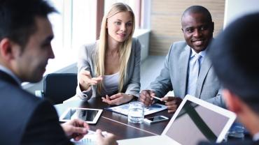four diverse professionals seated at a table smiling and having a discussion