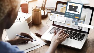 employee with back to viewer types on a computer screen showing open windows for a job search