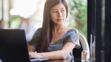 woman seated at her computer looking off in the distance contemplatively 