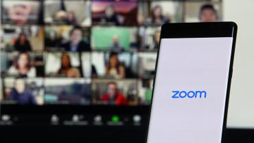 Phone with zoom logo in foreground, desktop zoom meeting in background
