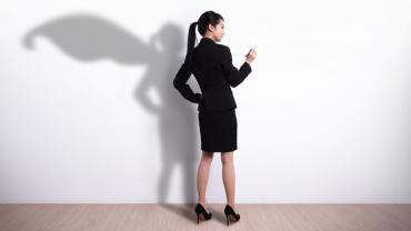 a standing woman in a suit with her shadow against a wall wears a superhero cape
