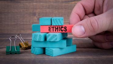 a hand stacks small blocks of one color and starts to pull another colored block with "Ethics" written on it. 