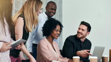 Group of diverse coworkers gathered around a laptop.