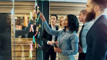 Group of diverse employees using colorful sticky notes in a bright office.