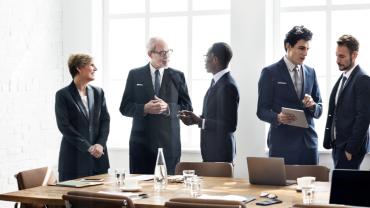 Group of diverse business people in sunny board room in front of a wood table.