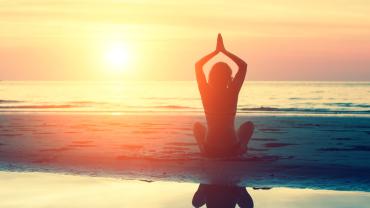 Silhouette of woman doing yoga on the beach during sunrise.