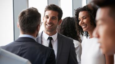 Group of diverse business people smiling and chatting in a brightly lit office.