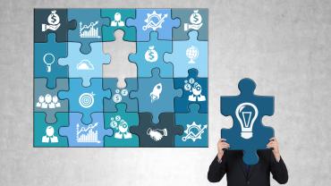 puzzle with different illustrations on each such as money bags, bar chart showing increases, hands shaking, with one missing piece, next to it person in suit, head covered by the missing piece with a lightbulb symbolizing idea