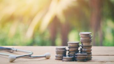 Close up of a stethoscope and stack of coins on an old wood table. 