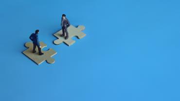 Two men facing each other on matching jigsaw pieces. 