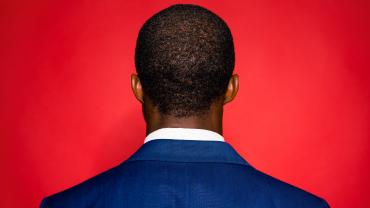 Man with his back turned towards a red background. 