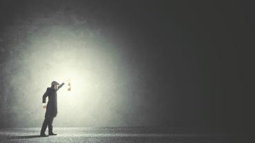 Man holding up a glowing lamp in the midst of darkness. 