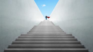 Image of stairs emerging from the ground, with an individual heroically standing at the top. 