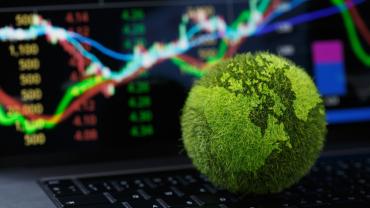 Green, grassy globe in front of a computer screen with stocks on it. 