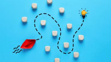 Origami ship navigating obstacles towards a glowing lightbulb. 