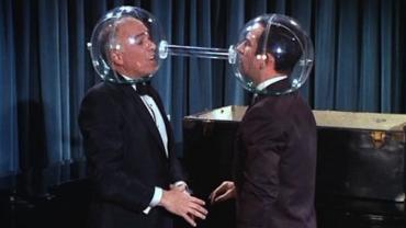 two men with plastic globes over their heads. they are facing one another and the globes are connected with a tube