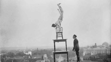 a man balancing in a handstand on top of stacked tables and chairs