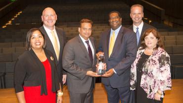 a group of 6 people standing on stage. 2 people in the middle are holding an award