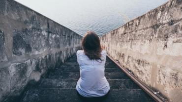an image of a person sitting on stone steps leading to a body of water