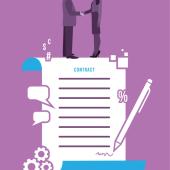 Two people stand on top of a contract and shake hands. 