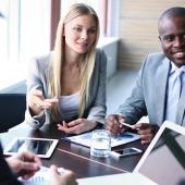 four diverse professionals seated at a table smiling and having a discussion