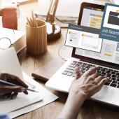 employee with back to viewer types on a computer screen showing open windows for a job search
