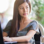 woman seated at her computer looking off in the distance contemplatively 