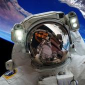 profile of an astronaut in space with the earth in the background. The astronauts face shield reflects the space station.