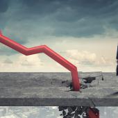 Red line chart plummeting into sidewalk next to a businessman in front of a cloudy gray sky.