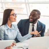 Group of diverse business professionals smiling and chatting in a sunny meeting room.