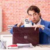 man, looks like, white or brown skin, stealing bag with dollar sign into portfolio case, wearing suit, in office setting