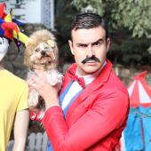 circus tent, clown, man, appears, white, holding dog, dressed like circus ringleader, his expression is like he is possibly in charge