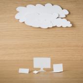 Paper cutout of computers under a cloud against a wooden table background. 