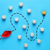 Origami ship navigating obstacles towards a glowing lightbulb. 