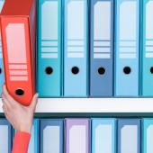 a hand choosing a red file from a shelf of blue files